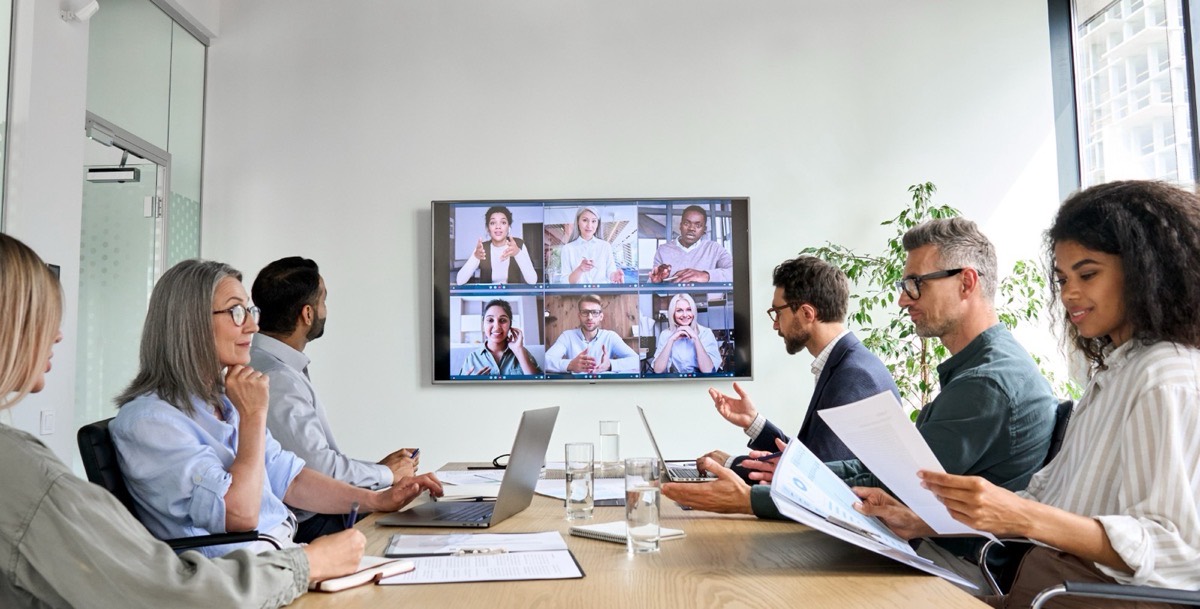 A conference room on a video call, the screen showing remote attendees
